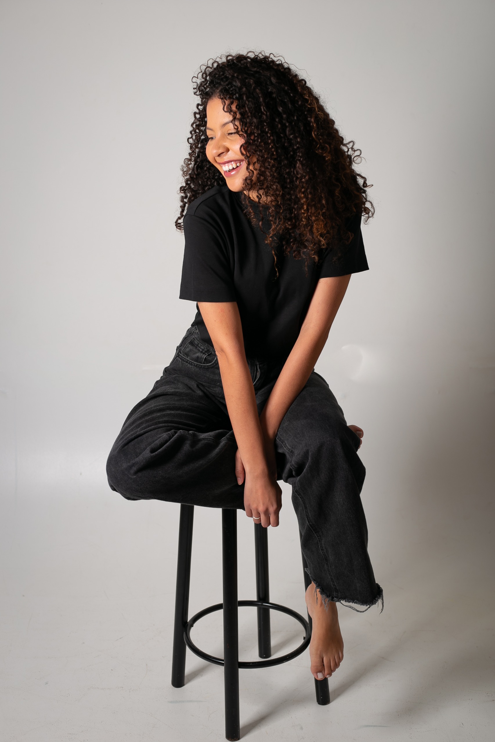 Mulher sorrindo, sentada em um banco, com roupa preta