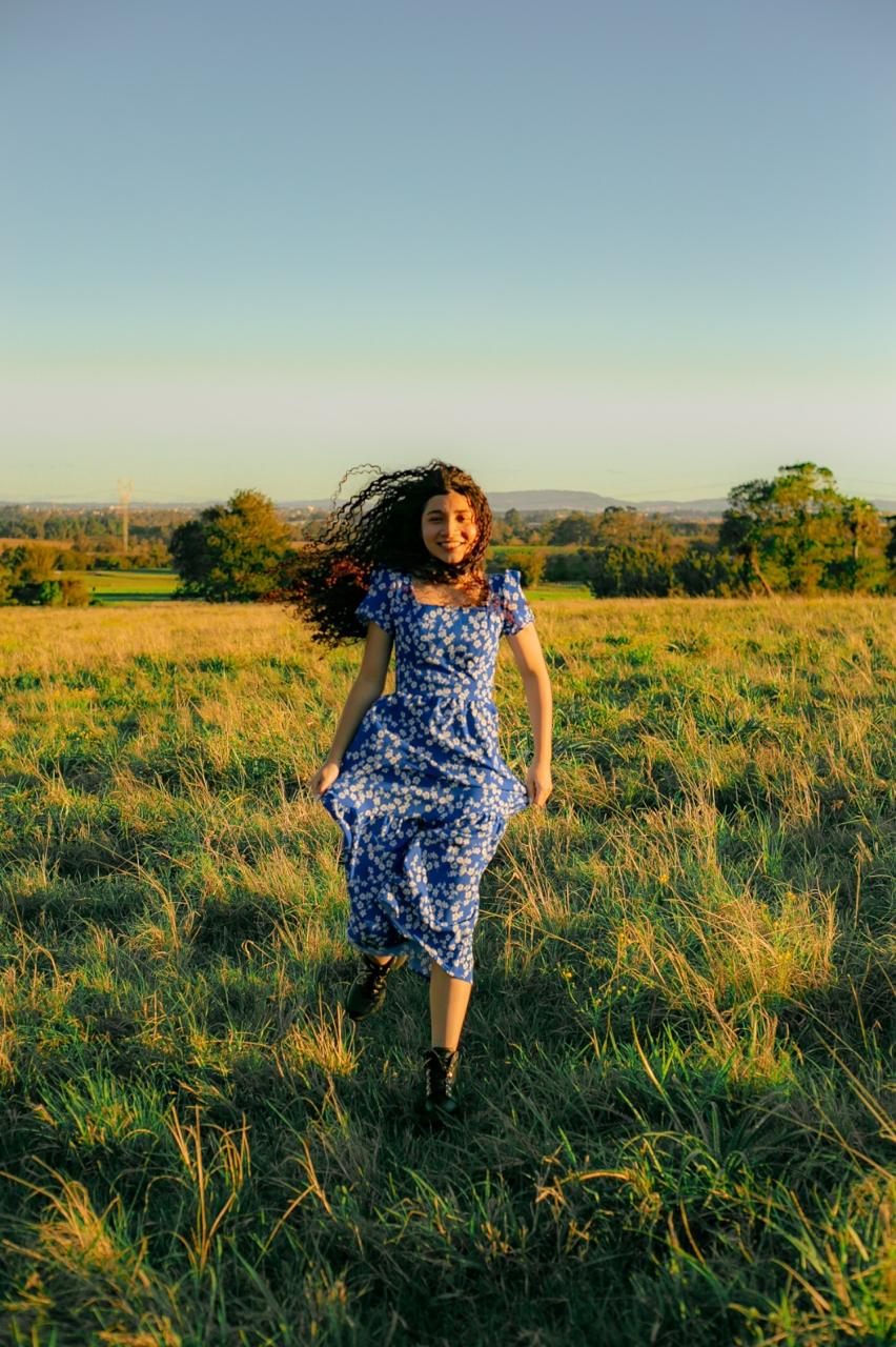 Jovem de vestido azul em movimento em um campo ao pôr do sol